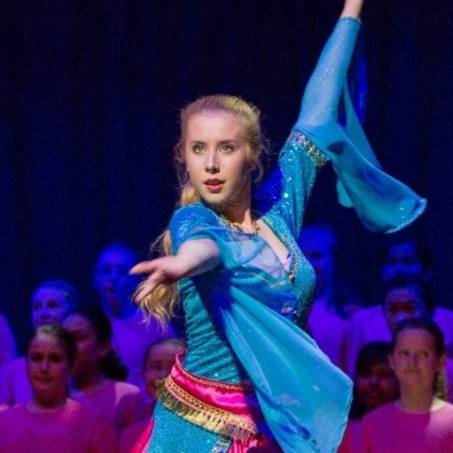 Grace performs a dance on stage in an Aladdin style outfit with her arms up