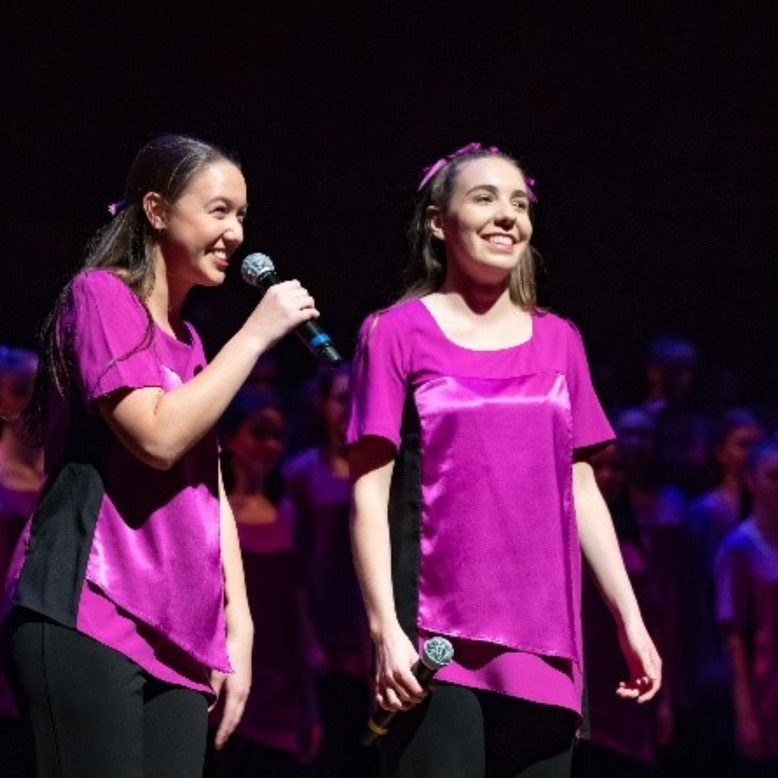 Alice laughs on stage under the spotlight while the girl next to her speaks