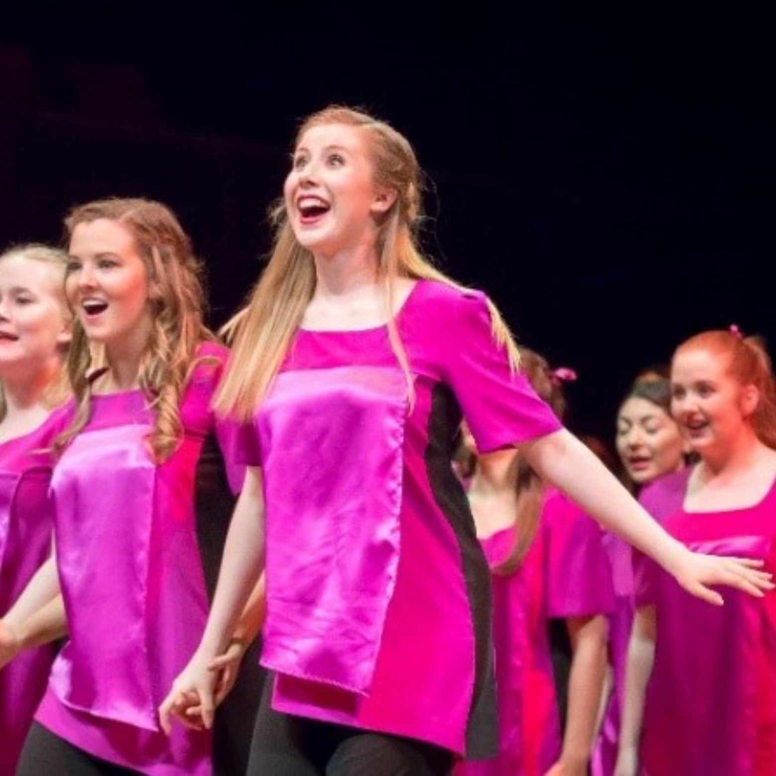 Grace performs with a bright smile on stage as part of a group number